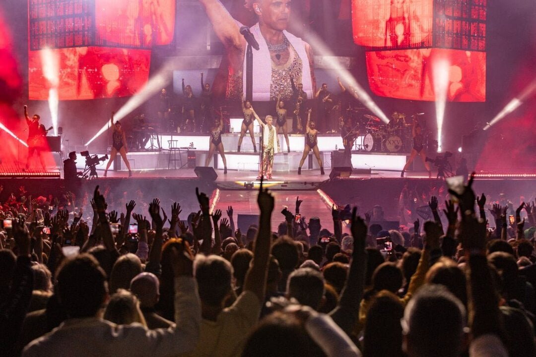 Robbie Williams en el escenario junto a un público entusiasta, disfrutando de su actuación llena de energía y emoción durante el concierto.