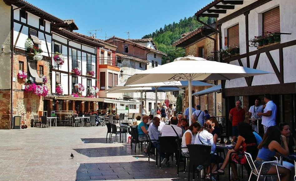 Zona de terrazas en las calles de Ezcaray en un día soleado, con gente disfrutando en los bares y la característica arquitectura del lugar como telón de fondo.